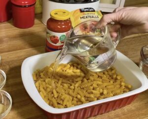 Add pasta and water to baking dish for Easy Dump and Bake Meatball Casserole