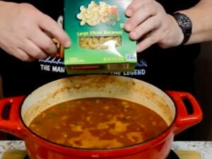 adding elbow macaroni to pot for goulash