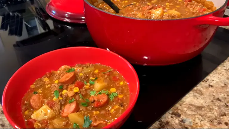 3 Meat Cowboy Stew in a red bowl next to a red dutch oven pot